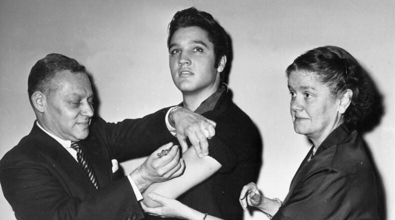 FILE - In this Oct. 28, 1956 file photo, Elvis Presley receives a Salk polio vaccine shot in New York City from Dr. Harold Fuerst, left. At right is Dr. Leona Baumgartner, commissioner of the New York City health department. Tens of millions of today's older Americans lived through the polio epidemic, their childhood summers dominated by concern about the virus. Some parents banned their kids from public swimming pools and neighborhood playgrounds and avoided large gatherings. Some of those from the polio era are sharing their memories with today's youngsters as a lesson of hope for the battle against COVID-19. Soon after polio vaccines became widely available, U.S. cases and death tolls plummeted to hundreds a year, then dozens in the 1960s, and to U.S. eradication in 1979.(AP Photo/File)