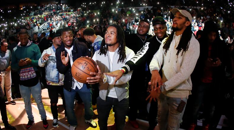 Atlanta Falcons running back Devonta Freeman (24) takes a shot as wide receiver Mohamed Sanu and cornerback Jalen Collins, right, joke with him as they are introduced during halftime of an NBA basketball game between the Washington Wizards and the Atlanta Hawks on Friday, Jan. 27, 2017, in Atlanta. Atlanta will face New England in Super Bowl 51. (AP Photo/John Bazemore)