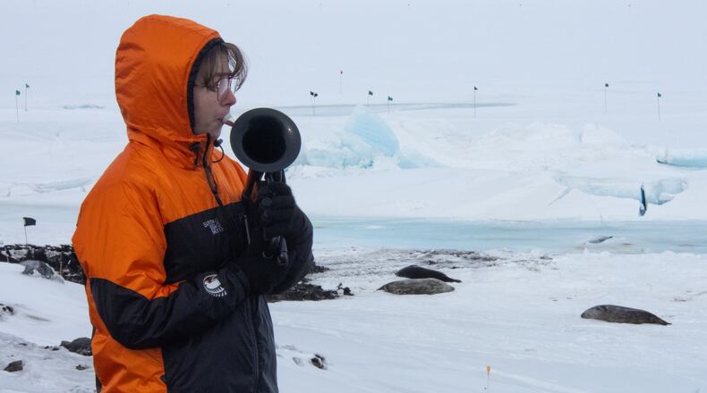 In this photo provided by Antarctica New Zealand, Natalie Paine plays a plastic French horn at Scott Base in Antarctica, on Nov. 16, 2025. (Anthony Powell/Antarctica New Zealand via AP)