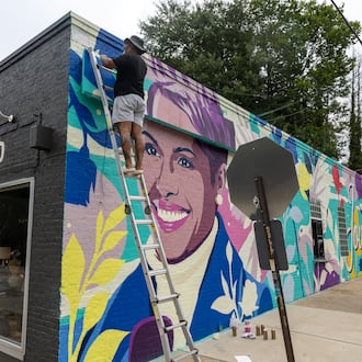 Artist Tommy Bronx (top) puts finishing touches on his new mural honoring the late news anchor Jovita Moore on the side of Bellwood Coffee in Atlanta on July 29, 2026. The coffee shop created community outcry when it painted over the original mural of Moore. (Arvin Temkar/AJC)