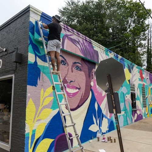 Artist Tommy Bronx (top) puts finishing touches on his new mural honoring the late news anchor Jovita Moore on the side of Bellwood Coffee in Atlanta on July 29, 2026. The coffee shop created community outcry when it painted over the original mural of Moore. (Arvin Temkar/AJC)