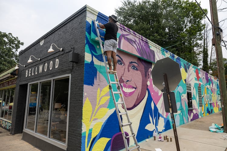 Artist Tommy Bronx (top) puts finishing touches on his new mural honoring the late news anchor Jovita Moore on the side of Bellwood Coffee in Atlanta on July 29, 2026. The coffee shop created community outcry when it painted over the original mural of Moore. (Arvin Temkar/AJC)