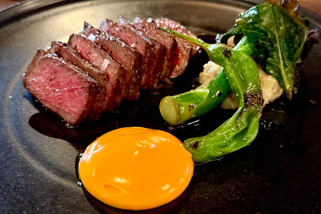A sliced steak with a side of Chinese broccoli and a bright orange chili sabayon sauce in a neat circle