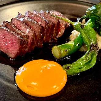 A sliced steak with a side of Chinese broccoli and a bright orange chili sabayon sauce in a neat circle