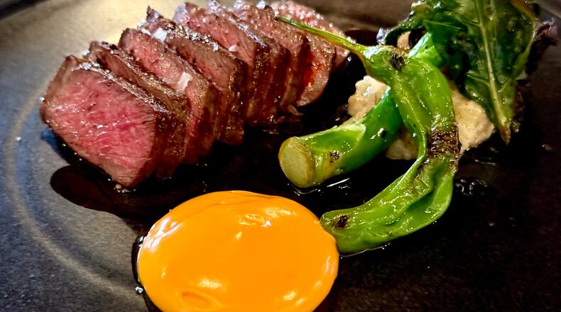 A sliced steak with a side of Chinese broccoli and a bright orange chili sabayon sauce in a neat circle