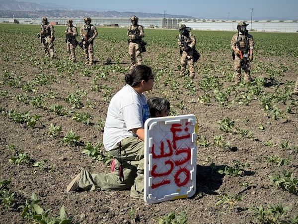 A demonstrator kneels in front of federal agents in a farm field during an immigration raid in Camarillo, Calif. (AP Photo/Michael Owen Baker)