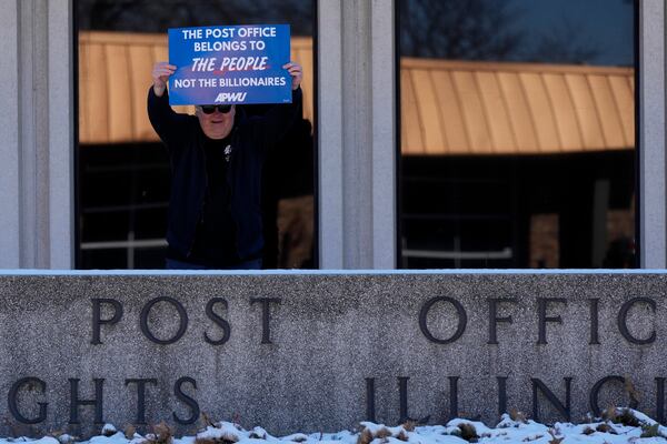 A man holds a sign during a demonstration outside of the United States Postal Service in Arlington Heights, Ill., Thursday, March 20, 2025. (AP Photo/Nam Y. Huh)