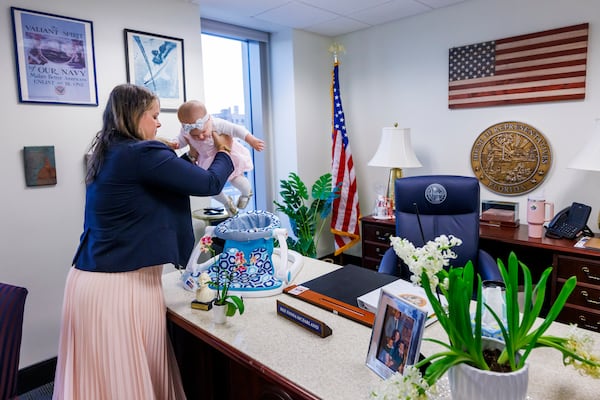 Florida Rep. Fiona McFarland, R-Sarasota, lifts her 7-month-old daughter Grace Melton into a chair on her desk as she starts her work day at the state Capitol, Thursday, April 17, 2025, in Tallahassee, Fla. (AP Photo/Colin Hackley)