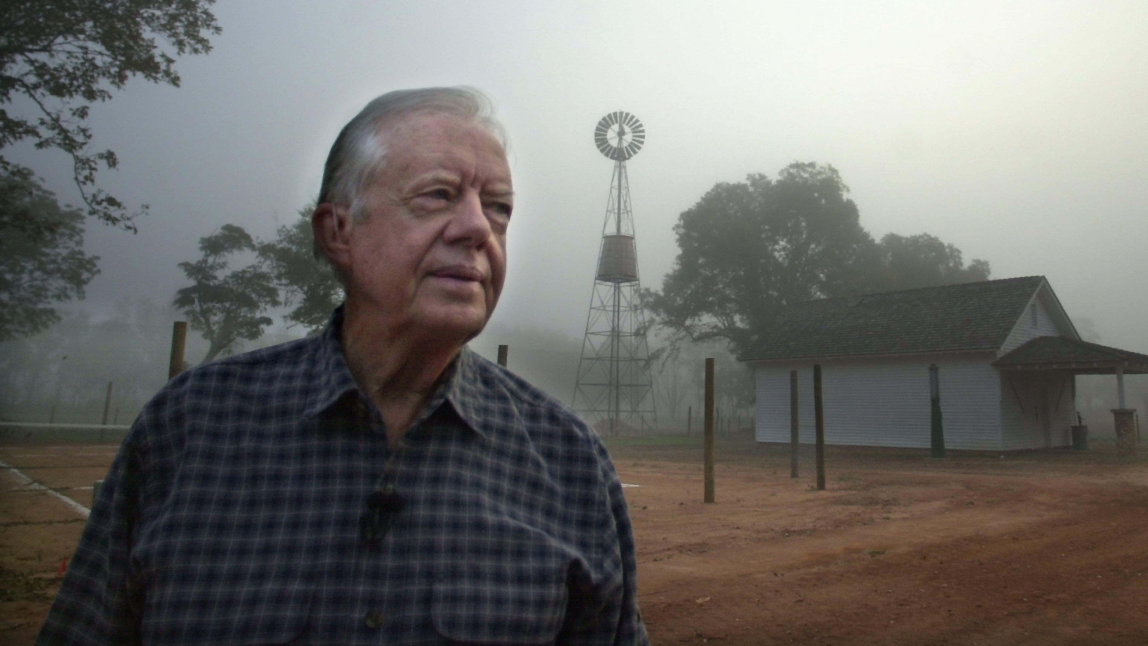 Former President Jimmy Carter looks over the site of his boyhood home and farm as a bank of fog lifts at day break near Plains, Ga., on Monday, Oct. 30, 2000. In the background is the family store and a windmill Carter's father erected in 1935 that supplied running water for the family for the first time. (Curtis Compton/AJC)