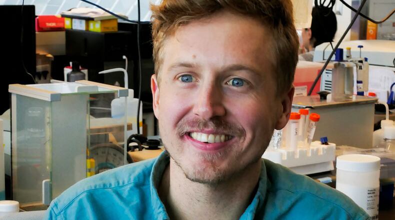 Portrait of Jordan Hamm, smiling at the camera. He has brown hair, a moustache, and is wearing a light blue, short sleeved button-up shirt.