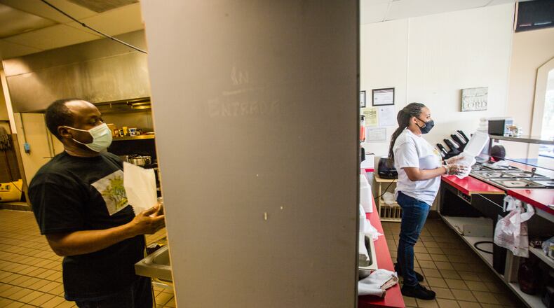 Businesses in this Hampton, GA strip mall are experiencing the effects of the pandemic differently. Floyd Johnson, left, works in the kitchen making soup and Chandra Johnson, right, fills a to-go order at Reggae Vybz on Tuesday, Sept. 8, 2020. The family-owned Caribbean restaurant is struggling to keep going without sit-in dining and delivery orders still lagging. (Jenni Girtman for The Atlanta Journal-Constitution)