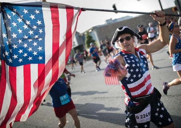 A man runs with an American flag as he makes his way down Peachtree Street during the 48th AJC Peachtree Road Race. (BRANDEN CAMP/SPECIAL)