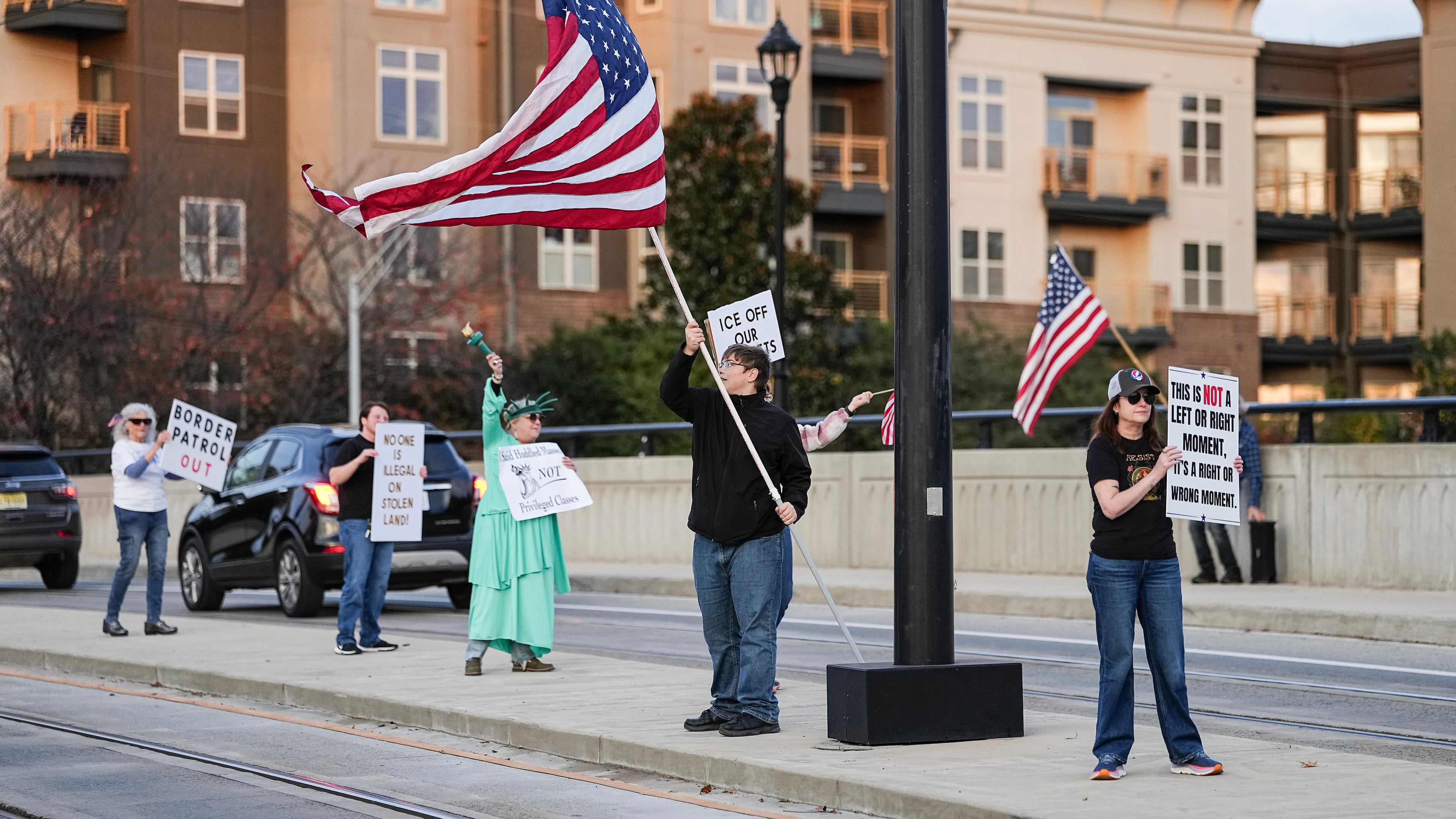 Protesters hold signs and flags amidst the arrival of federal law enforcement, Tuesday, Nov. 18, 2025, in Charlotte, N.C. (AP Photo/Matt Kelley)