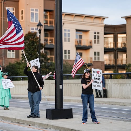 Protesters hold signs and flags amidst the arrival of federal law enforcement, Tuesday, Nov. 18, 2025, in Charlotte, N.C. (AP Photo/Matt Kelley)