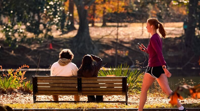 A woman walks past a couple sitting inside Piedmont Park. Tuesday, December 19th, 2023 (Ben Hendren for the Atlanta Journal Constitution)