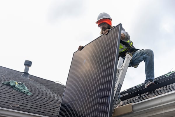Joe McClain, an installer for Creative Solar USA, moves solar panels onto the roof of a home in Ball Ground, Georgia, on December 17th, 2021. (Nathan Posner for The Atlanta Journal-Constitution)