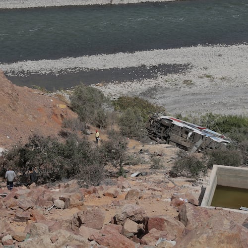 People walk by a passenger bus after its deadly crash with another vehicle in Arequipa, Peru, Wednesday, Nov. 12, 2025. (AP Photo/Kiara Tapia)