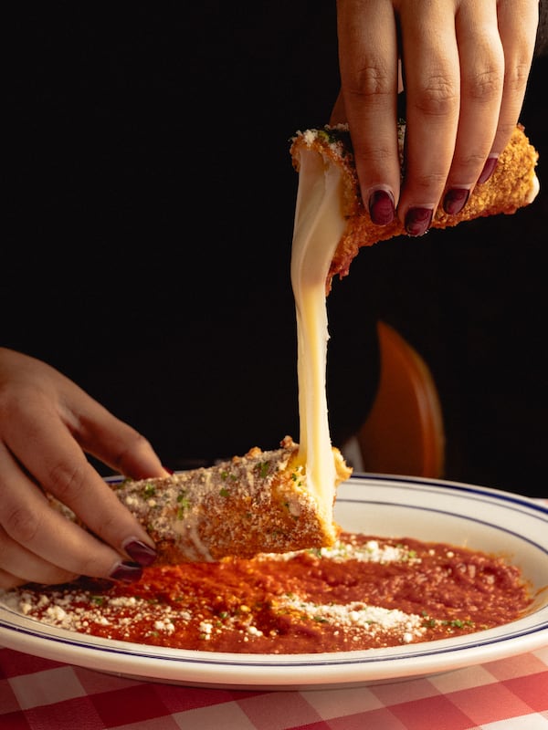 A huge mozarella stick being pulled apart over a bed of marinara sauce