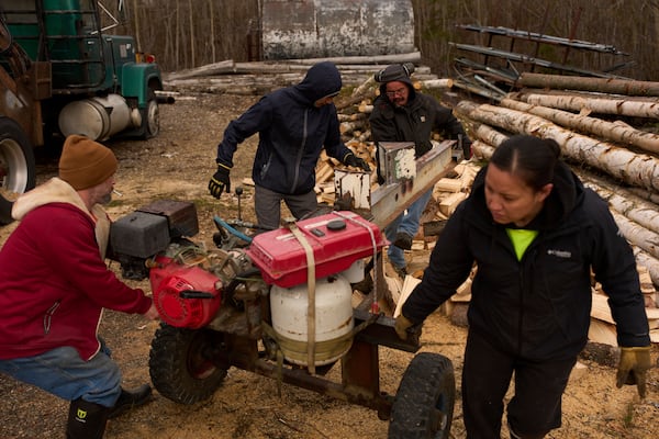 Workers with the Sustainable Energy for Galena, Alaska, from left, James Strong, Nathan Moses, Morris Demoski and Marissa McCarty move a log splitting machine before cutting wood to deliver to elders in the community Monday, May 19, 2025, in Galena. (AP Photo/John Locher)
