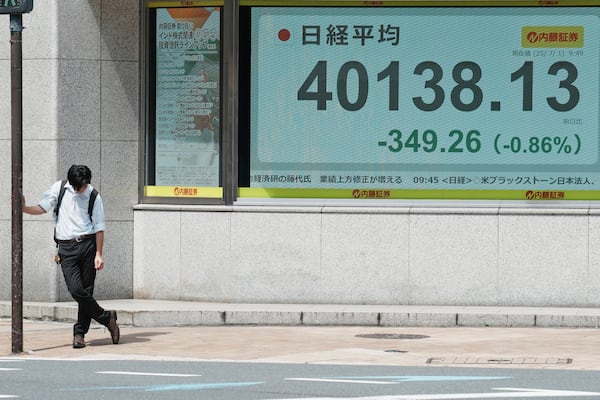 A person rests under the intense sun near an electronic stock board displaying Japan's Nikkei index at a securities firm Tuesday, July 1, 2025, in Tokyo. (AP Photo/Eugene Hoshiko)