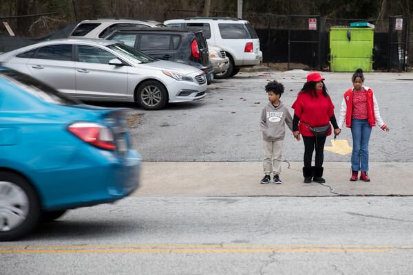 District 12 resident Joyce Smith hold the hands of her grandchildren as they cross the street on Browns Mill Road in south Atlanta. (Riley Bunch/AJC)