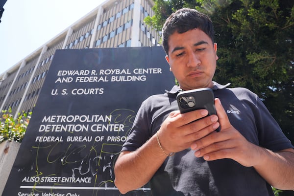 Alejandro Barranco checks his phone as he arrives to check on his father Narciso, who was detained by federal agents, outside the Metropolitan Detention Center on Monday, June 23, 2025, in Los Angeles. (AP Photo/Damian Dovarganes)