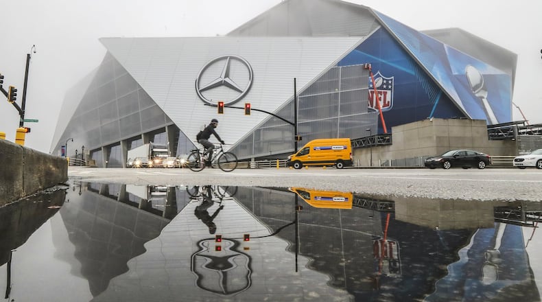Work continued on Mercedes-Benz Stadium adhering Super Bowl graphics across the facade reflected in puddled water along Martin Luther King Jr. Drive in downtown Atlanta. A group of residents claims the stadium should be paying property taxes. JOHN SPINK/JSPINK@AJC.COM