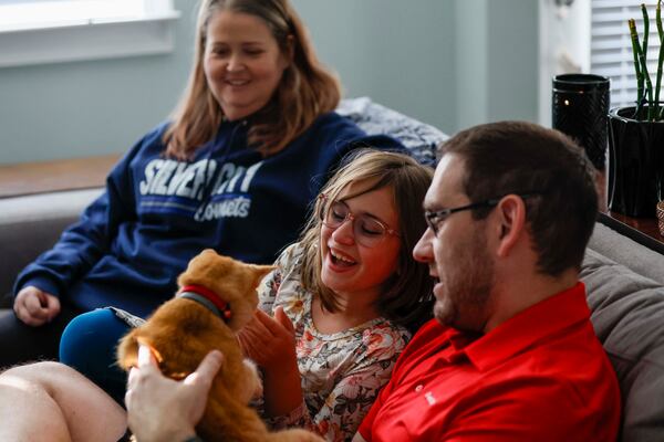(From left) Angela watchs as her 9-year-old daughter Avery and husband Daniel play with Dilly, one of their cats, at their Cumming home earlier in November. (Miguel Martinez/AJC)