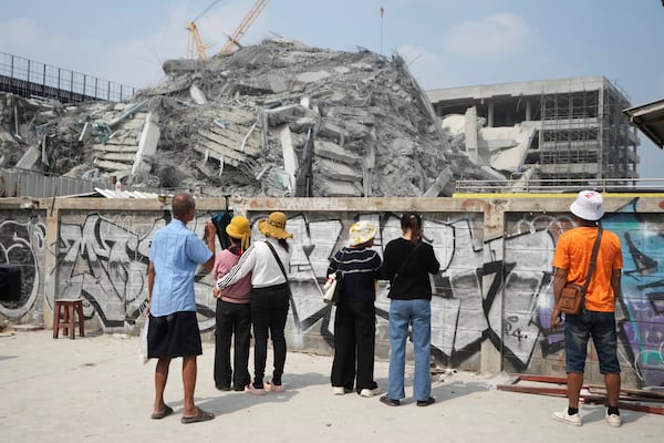 People stand near a damaged construction site of a high-rise building in Bangkok, Thailand, Saturday, March 29, 2025, as rescuers search for victims following its collapse after Friday's earthquake. (AP Photo/Sakchai Lalit)