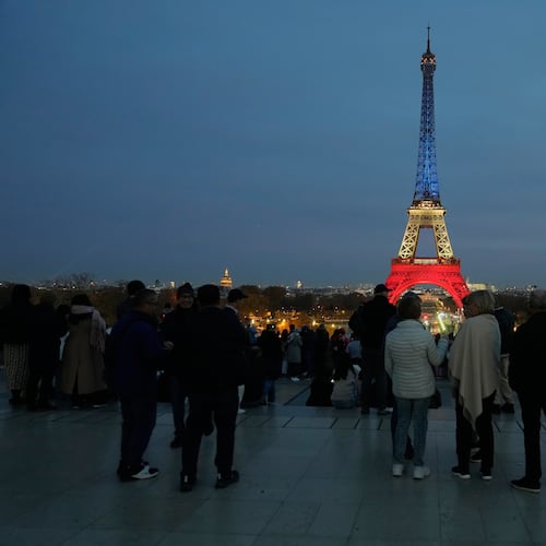 People gather at Trocadero Plaza as the Eiffel Tower is lit in the colors of the French national flag in Paris, Wednesday, Nov. 12, 2025, to honor the victims of the terror attacks at the Bataclan concert hall, cafes, and the national stadium 10 years ago. (AP Photo/Michel Euler)