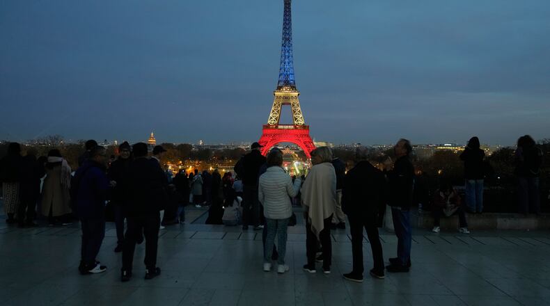 People gather at Trocadero Plaza as the Eiffel Tower is lit in the colors of the French national flag in Paris, Wednesday, Nov. 12, 2025, to honor the victims of the terror attacks at the Bataclan concert hall, cafes, and the national stadium 10 years ago. (AP Photo/Michel Euler)