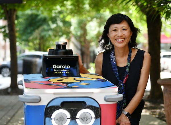 M.J. Burk Chun, co-founder & VP of product and design at Serve Robotics, poses next to their new food delivery robot “Darcie” outside Rreal Tacos' Midtown location, Thursday, June 26, 2025, in Atlanta. The robot was painted by Atlanta muralist George F. Baker III. (Hyosub Shin/AJC)