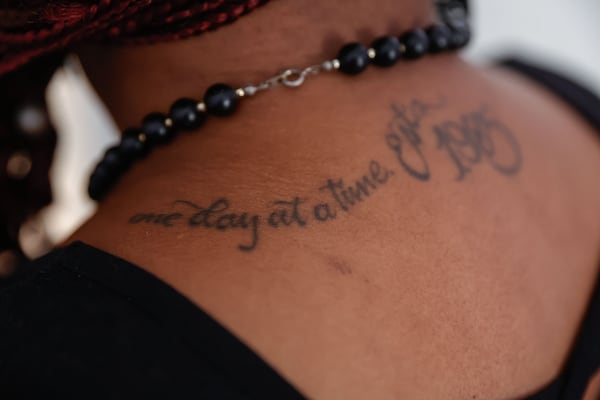 Tonisha Hines shows off a tattoo on her back that reads "one day at a time" at her apartment in Scottdale, Georgia, on Tuesday, Aug. 12, 2025. She said she's in 12-step recovery and has not used crack cocaine, her drug of choice, in nearly a decade. (Natrice Miller/ AJC) 