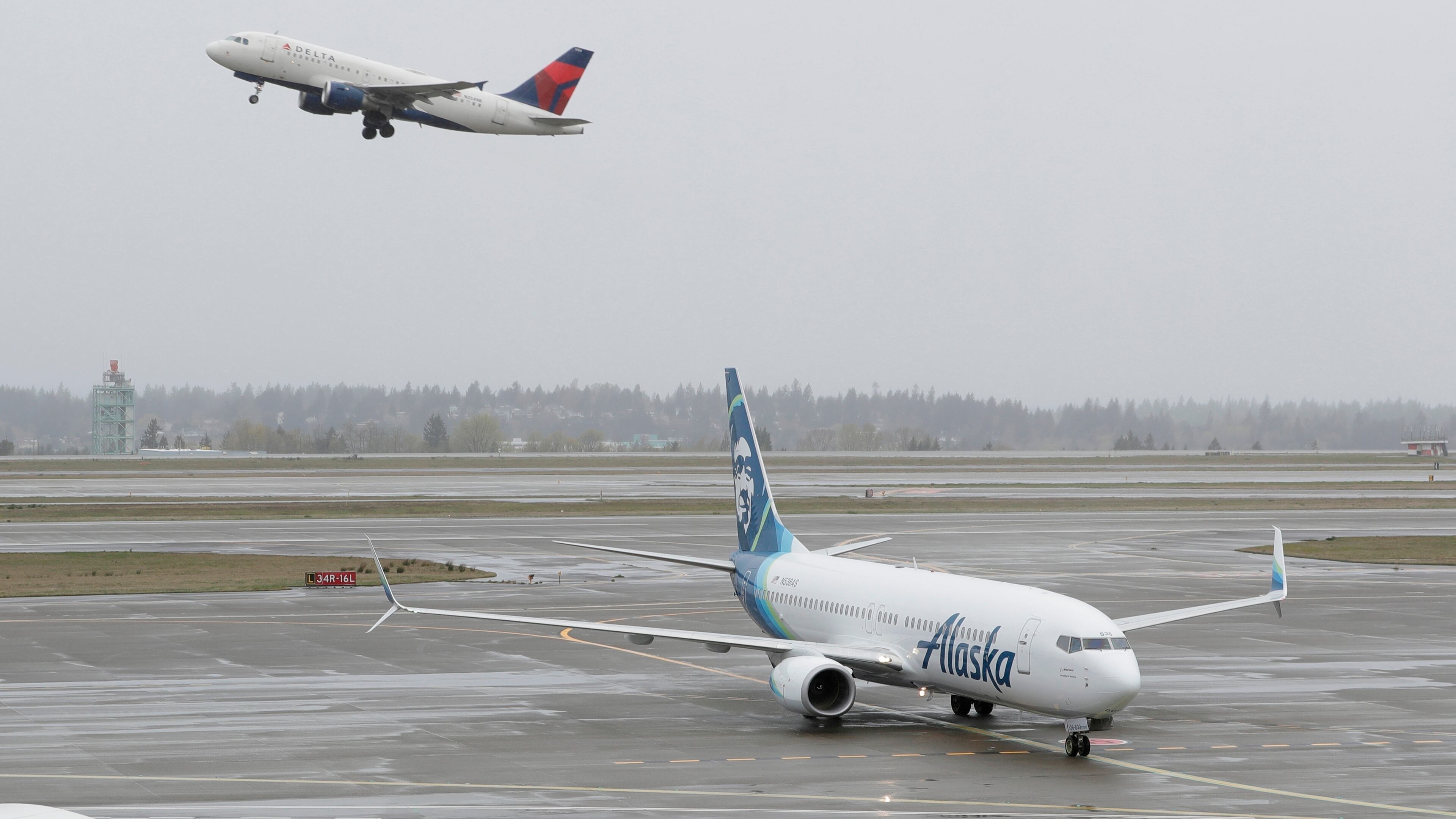 A Delta Air Lines plane takes off above a taxiing Alaska Airlines airplane at the Seattle-Tacoma International Airport in Seattle. The two airlines have become fierce competitors in the Seattle market. (Ted S. Warren/AP 2018)