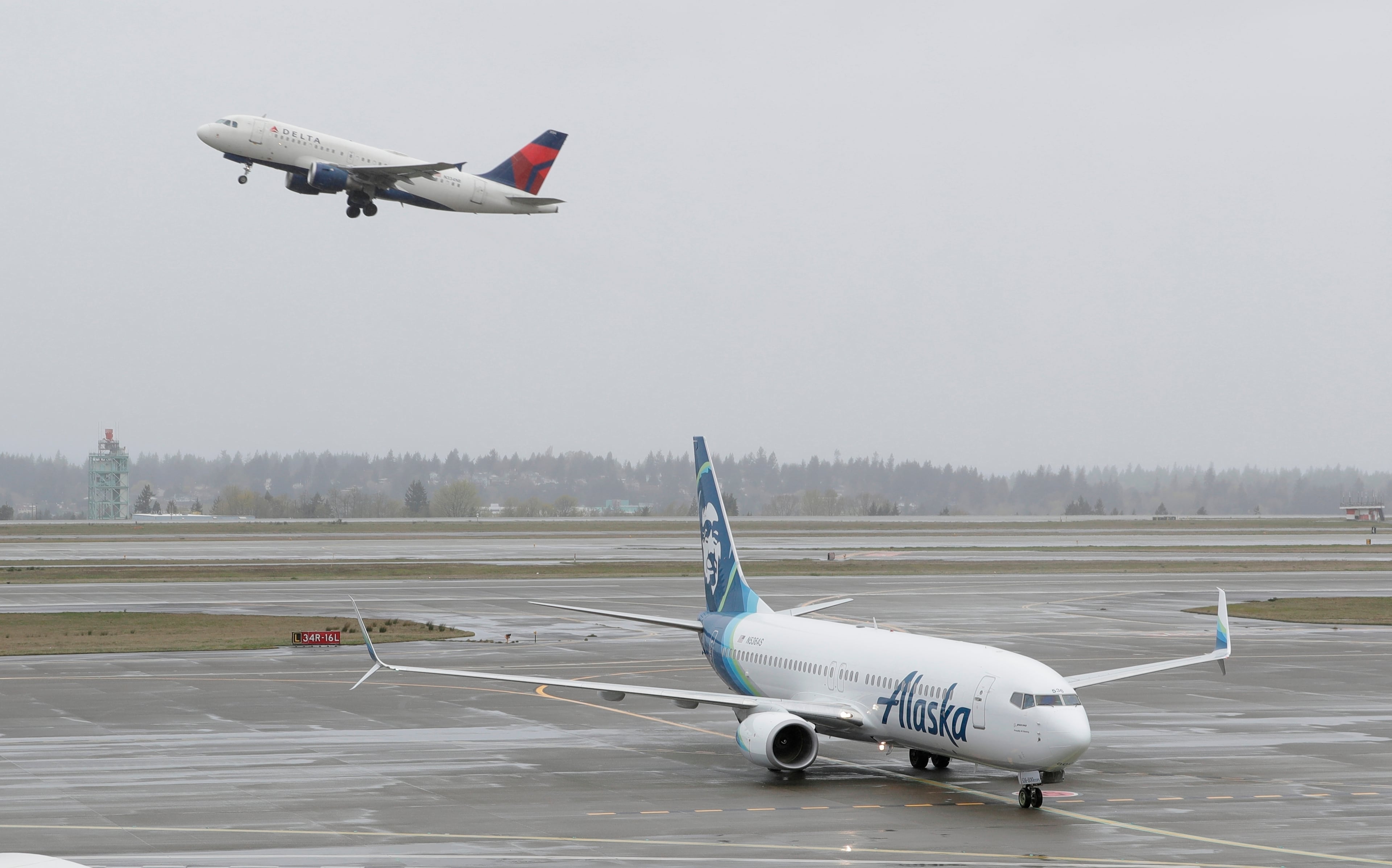 A Delta Air Lines plane takes off above a taxiing Alaska Airlines airplane at the Seattle-Tacoma International Airport in Seattle. The two airlines have become fierce competitors in the Seattle market. (Ted S. Warren/AP 2018)
