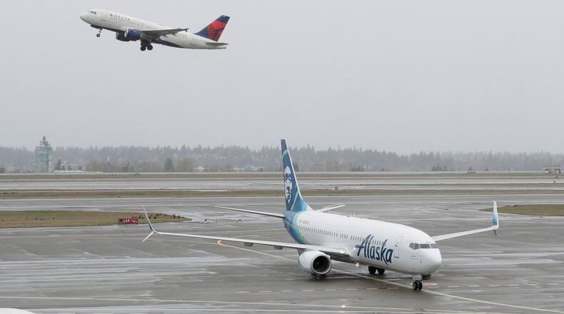 FILE - In this April 13, 2018 file photo, a Delta Air Lines plane takes off above a taxiing Alaska Airlines airplane at the Seattle-Tacoma International Airport in Seattle. U.S. airlines are asking the federal government for grants, loans and tax relief that could easily top $50 billion to help them recover from a sharp downturn in travel due to the new coronavirus. Airlines for America, the trade group representing the carriers, posted its request for financial help on Monday, March 16, 2020 just as more airlines around the world were announcing ever-deeper cuts in service and, in some cases, layoffs.