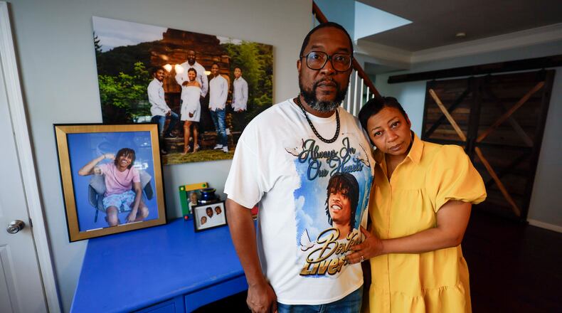 Ramonne and Terrica Thomas stand in the living room of their Mableton home, surrounded by images of their son, Boston Thomas, who was killed in May 2024 when a Cobb County police officer used a PIT maneuver to end a high-speed chase. The parents have filed a lawsuit against the county. (Miguel Martinez/AJC)