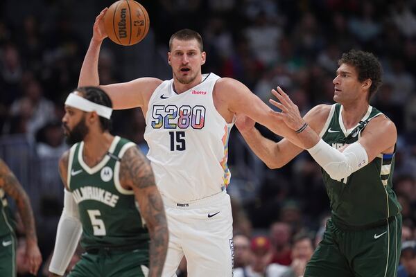 Denver Nuggets center Nikola Jokic, left, fields a pass as Milwaukee Bucks center Brook Lopez defends in the first half of an NBA basketball game Wednesday, March 26, 2025, in Denver. (AP Photo/David Zalubowski)