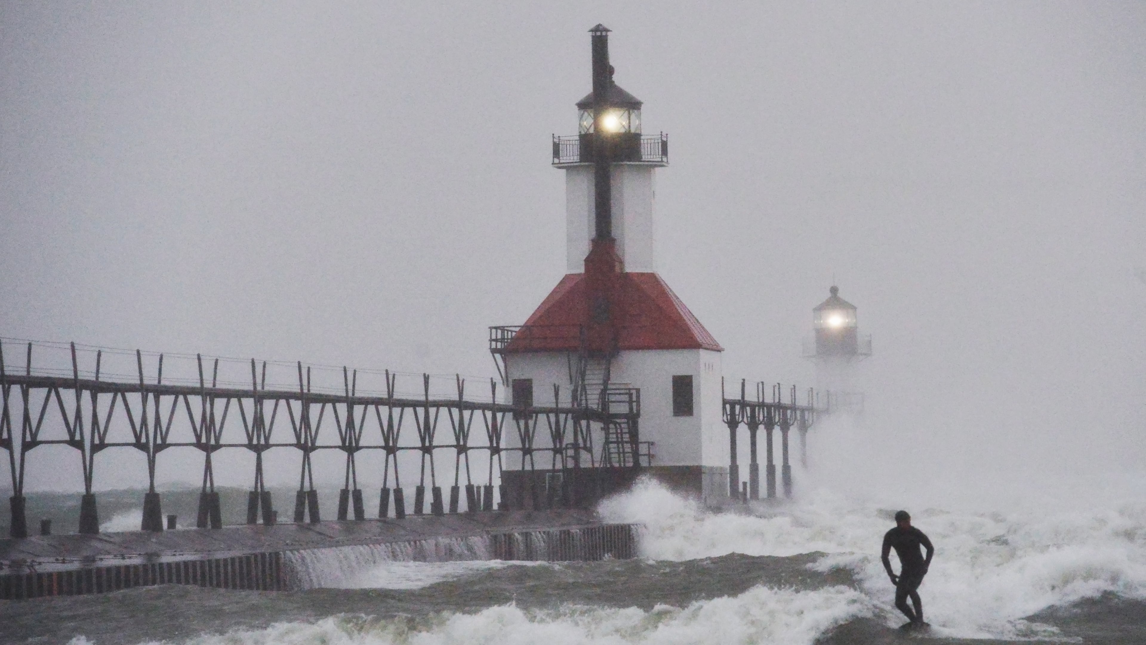 A surfer rides through blowing snow as Lake Michigan waves crash into the St. Joseph Inner and Outer Lighthouses Wednesday, Nov. 26, 2025, in St. Joseph, Mich. (Don Campbell/The Herald-Palladium via AP)