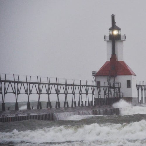 A surfer rides through blowing snow as Lake Michigan waves crash into the St. Joseph Inner and Outer Lighthouses Wednesday, Nov. 26, 2025, in St. Joseph, Mich. (Don Campbell/The Herald-Palladium via AP)