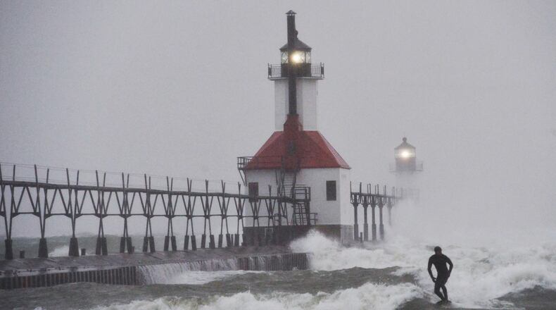 A surfer rides through blowing snow as Lake Michigan waves crash into the St. Joseph Inner and Outer Lighthouses Wednesday, Nov. 26, 2025, in St. Joseph, Mich. (Don Campbell/The Herald-Palladium via AP)