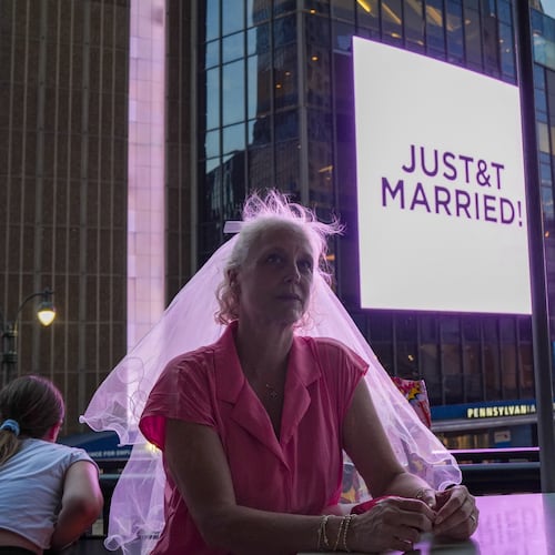 A Taylor Swift fan wearing a wedding veil sits at a restaurant next to Madison Square Garden where a "JUST&T MARRIED" sign is displayed during a wedding between singer Taylor Swift and National Football League player Travis Kelce on Friday, July 3, 2026, in New York. (AP Photo/Ryan Murphy)