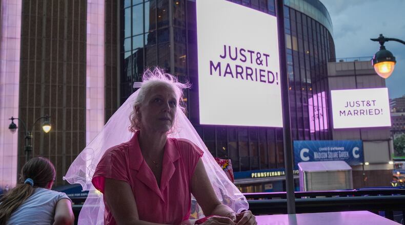 A Taylor Swift fan wearing a wedding veil sits at a restaurant next to Madison Square Garden where a "JUST&T MARRIED" sign is displayed during a wedding between singer Taylor Swift and National Football League player Travis Kelce on Friday, July 3, 2026, in New York. (AP Photo/Ryan Murphy)