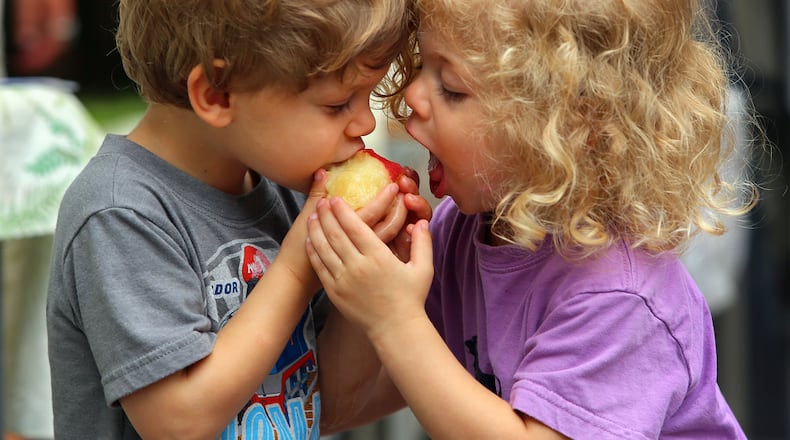 A PIECE OF THE PEACH--062313 ATLANTA Twins Oliver & Violet Webb, 3, Decatur, share a Watsonia organic peach from South Carolina at the Watsonia tent during a trip with their grandfather Marc Taub to the Grant Park Farmer's Market on Sunday, June 23, 2013, in Atlanta. Georgia has been whipped by South Carolina in the peach wars, but the succulent fruit still serves as an emblem for the state and it's even on our "I Voted" stickers. CURTIS COMPTON / CCOMPTON@AJC.COM