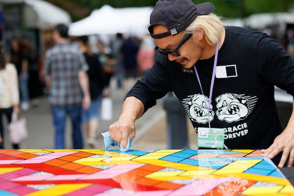 Mix-media artist John Ha from California cleans a piece as festival goers walk by during the 2023 Atlanta Dogwood Festival. The festival may have to change its business model to survive. 
(Miguel Martinez/AJC)