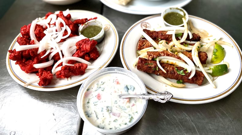 This takeout feast from Cafe Bombay includes (clockwise from top): goat biryani, Goan shrimp curry, lamb seekh kebabs, raita and Chicken 65. Wendell Brock for The Atlanta Journal-Constitution