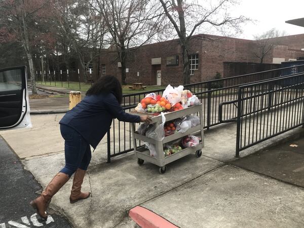 Jasmine Crowe, founder of Goodr, pushes a cart full of fruit into Phoenix Academy, the former Crim High School, on Monday to prepare for the first day of food distribution at Atlanta Public Schools. Goodr partnered with APS to set up sites for students to get food while school buildings are closed. VANESSA McCRAY/AJC