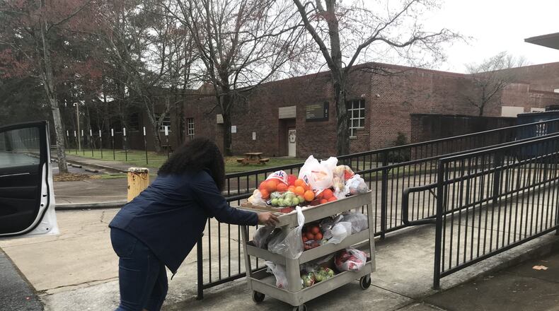 Jasmine Crowe, founder of Goodr, pushes a cart full of fruit into Phoenix Academy, the former Crim High School, on Monday to prepare for the first day of food distribution at Atlanta Public Schools. Goodr partnered with APS to set up sites for students to get food while school buildings are closed. VANESSA McCRAY/AJC