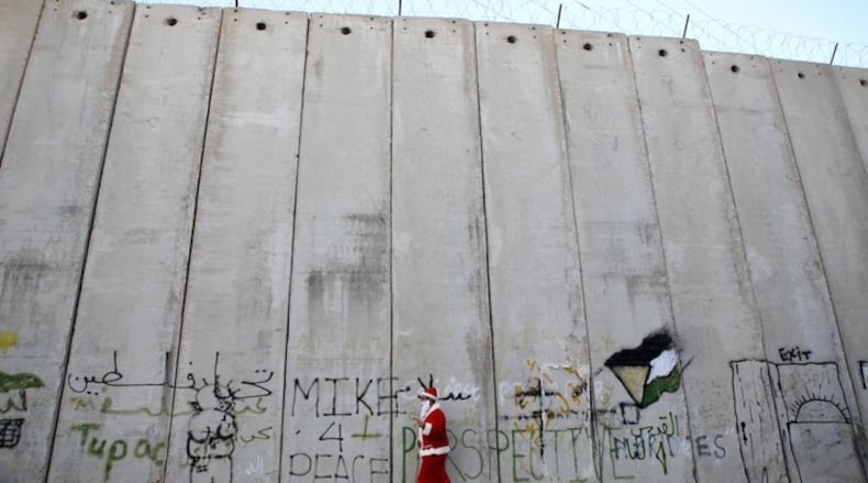A Palestinian man dressed as Santa Claus walks near the controversial Israeli separation barrier in the West Bank village of Bir Nabala, between Jerusalem and Ramallah, in a December 2014 file image. (Shadi Hatem/APA Images/Zump Press/TNS)