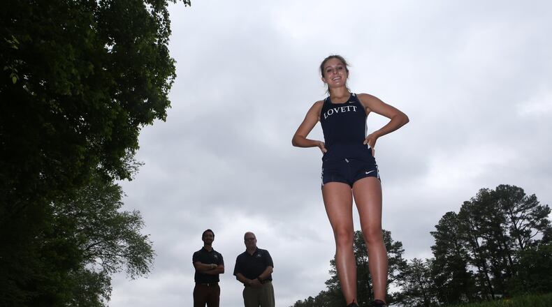 Serena Tripodi (right) poses for a portrait with her coaches Jimmy Jewell (center) and Chris Mayer (left) in the background at The Lovett School in Atlanta, Georgia, on May 4, 2017. Tripodi holds seven state titles in track and cross country, with five of those being individual. (HENRY TAYLOR / HENRY.TAYLOR@AJC.COM)